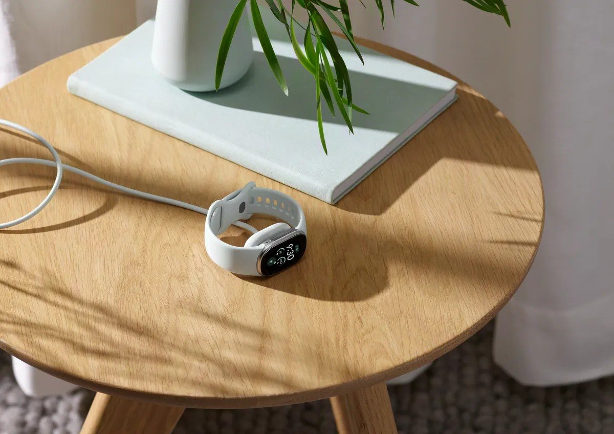 Fitbit Edge albă pe încărcătorul magnetic, pe o masă de lemn